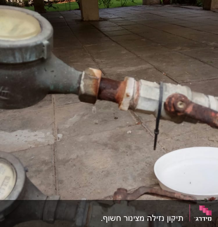 מד מים חלוד עם צינור וברז על רצפה